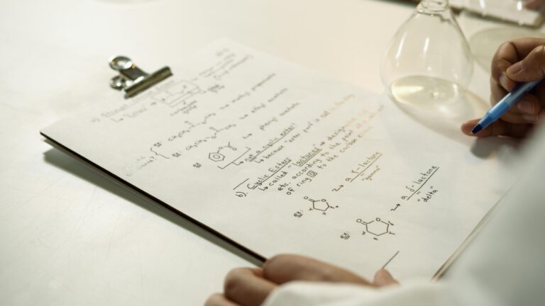 A close-up view of handwritten chemical formulas on a clipboard in a lab setting.